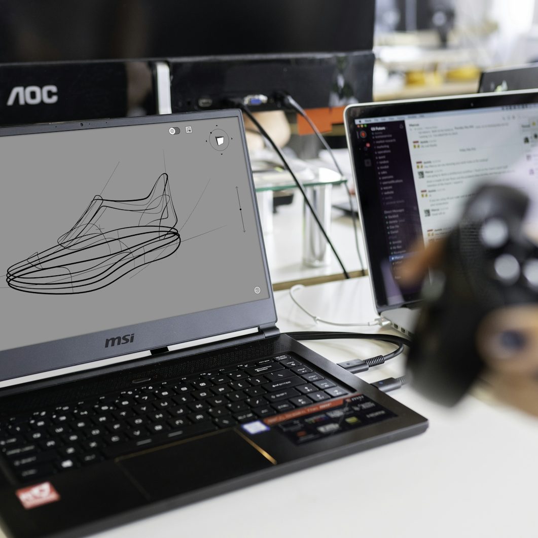 Entwurf eines Sportschuhs auf einem Laptop-Bildschirm, daneben ein weiterer Laptop.